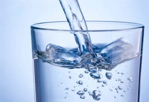 close-up-pouring-water-into-glass-on-blue-background